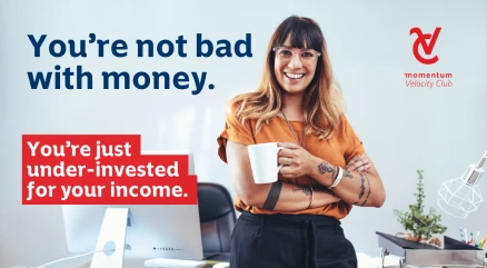 A successful female professional leaning against her office desk, with coffee in hand, smiling confidently.